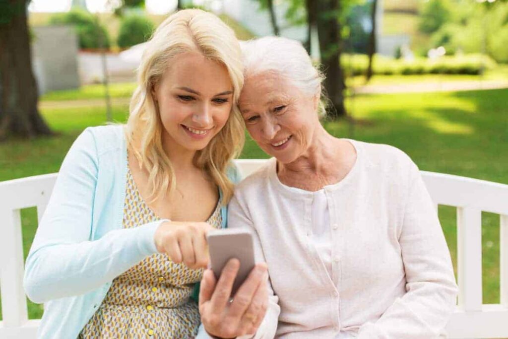 Senior woman sitting outdoors on a bench with her daughter looking at information for Traditions of Medina on a smartphone