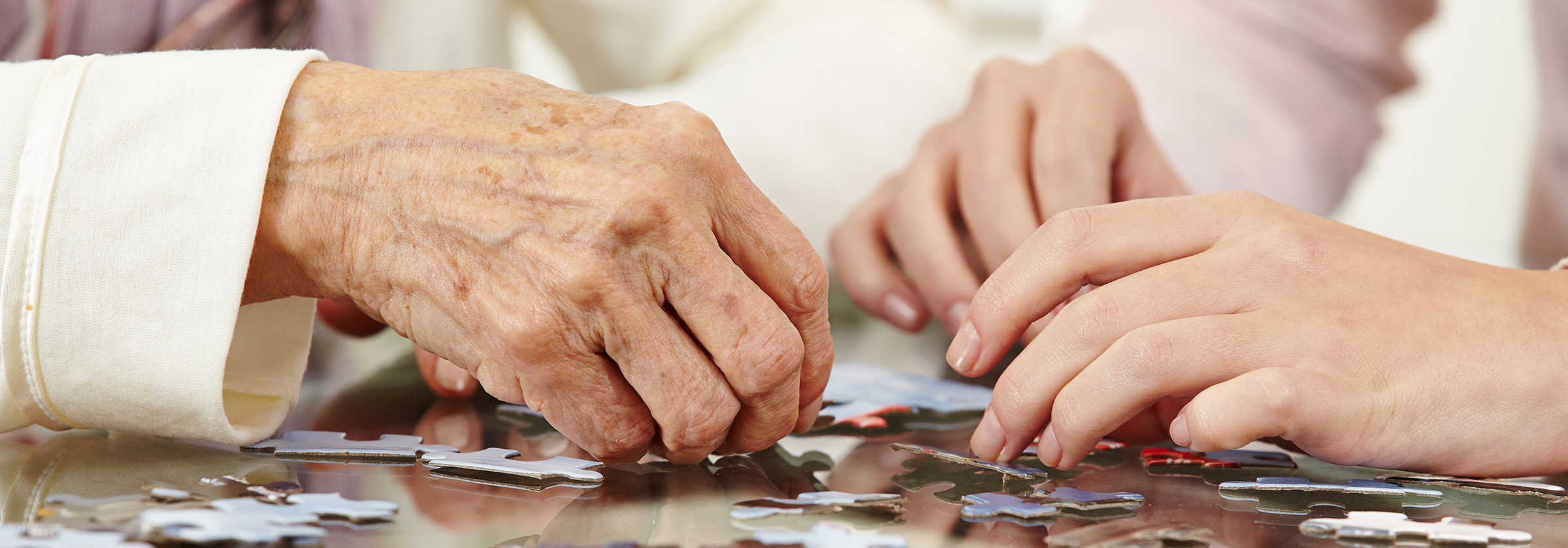Close up photo of a senior person's hands and a younger person's hands as they put together puzzle pieces